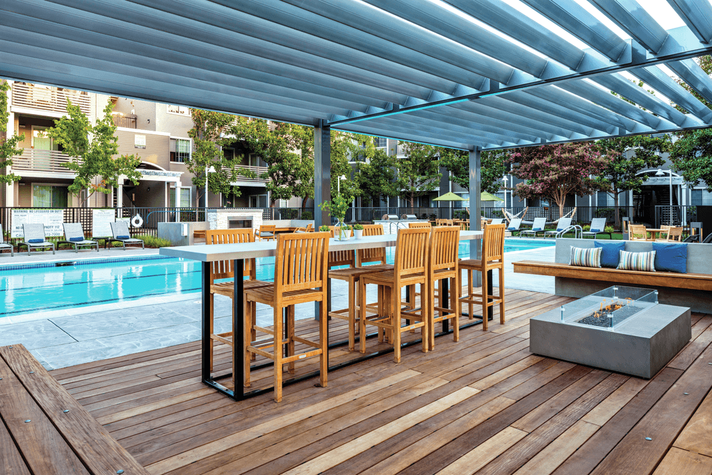 A wooden table and chairs are set up on a deck under a blue canopy.