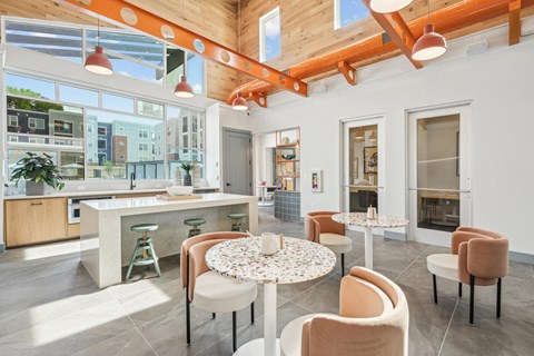 a communal area with tables and chairs and a kitchen with large windows