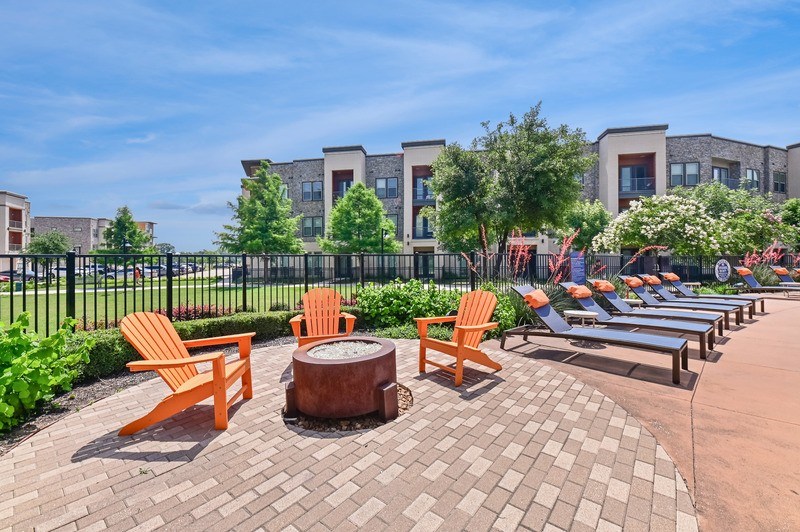 A sunny day at a park with orange chairs and a fire pit.
