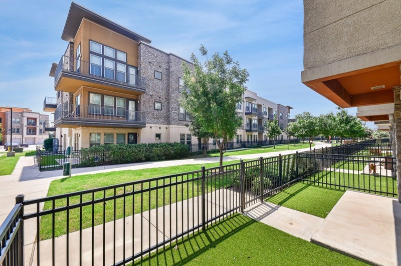 A modern apartment complex with a black fence and green lawns.