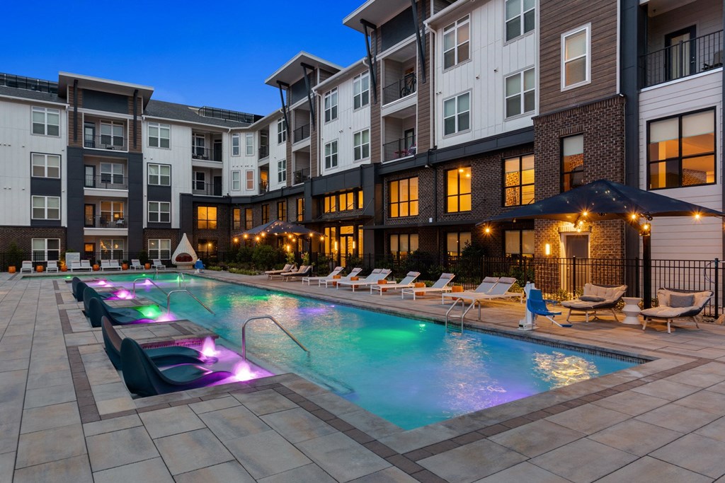 A large swimming pool with lounge chairs and a lit-up fountain in the middle.