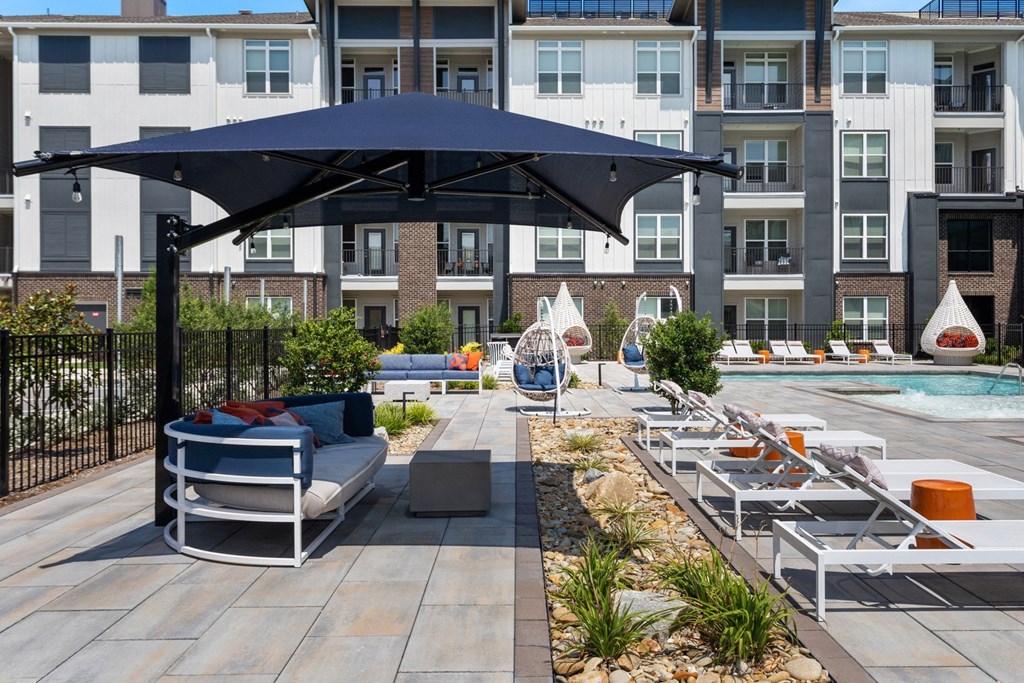 A patio with a black umbrella and white furniture.