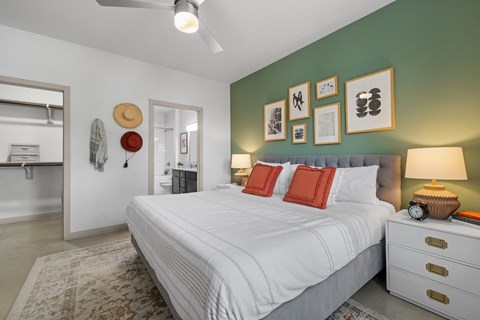 A bedroom with a white bed, a hat hanging on the wall, and a ceiling fan.