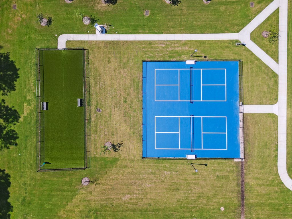 An aerial view of a tennis court surrounded by a green field.