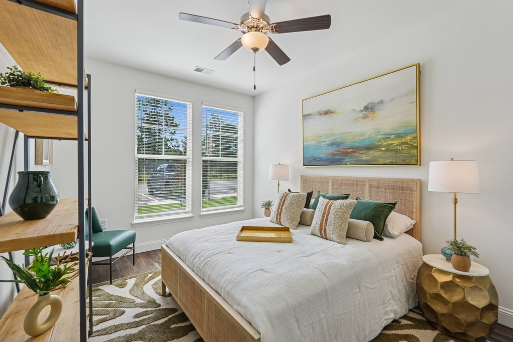 A bedroom with a bed, a ceiling fan, and a painting on the wall.