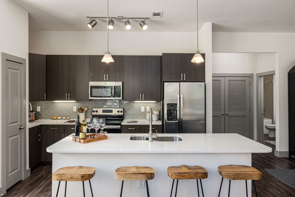 a kitchen with a large white island with three wooden stools