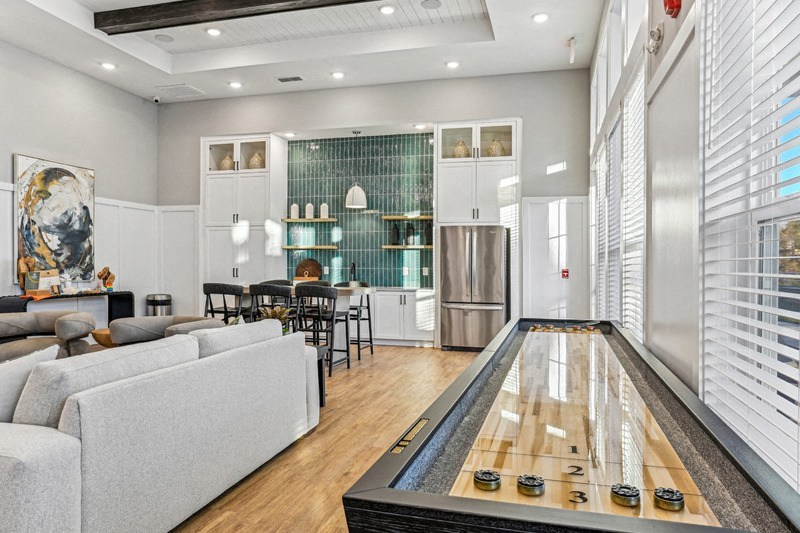 A shiny wooden pool table is in the middle of a well-lit room with a couch and a dining table.