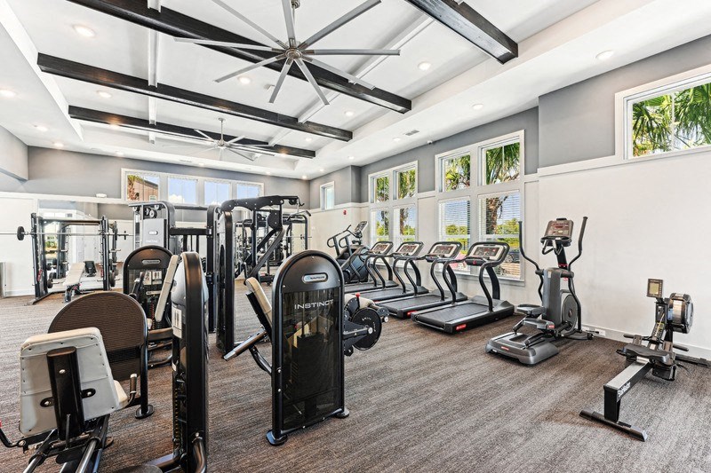 a gym with cardio machines and other exercise equipment in a room with windows