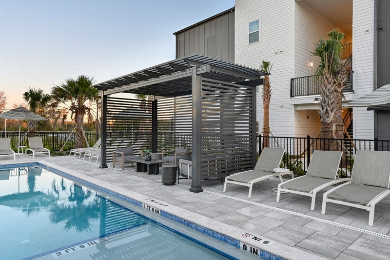 A pool with a sun shade and lounge chairs.