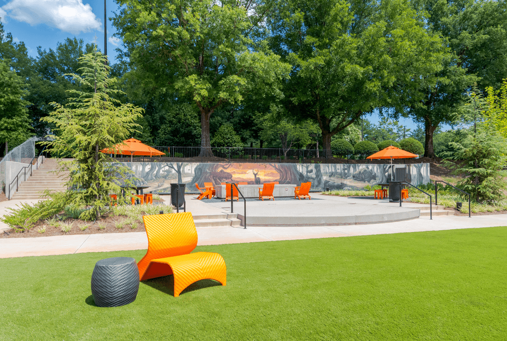 A park with orange chairs and a black tire on the grass.