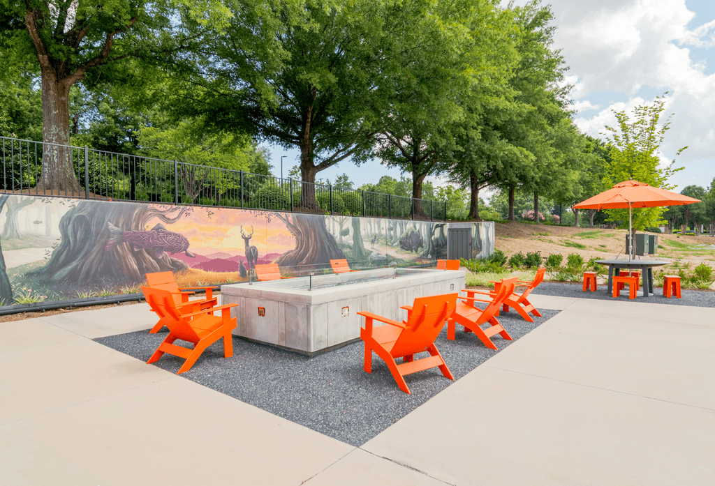 A mural of a desert scene is painted on a wall next to orange chairs and a table.