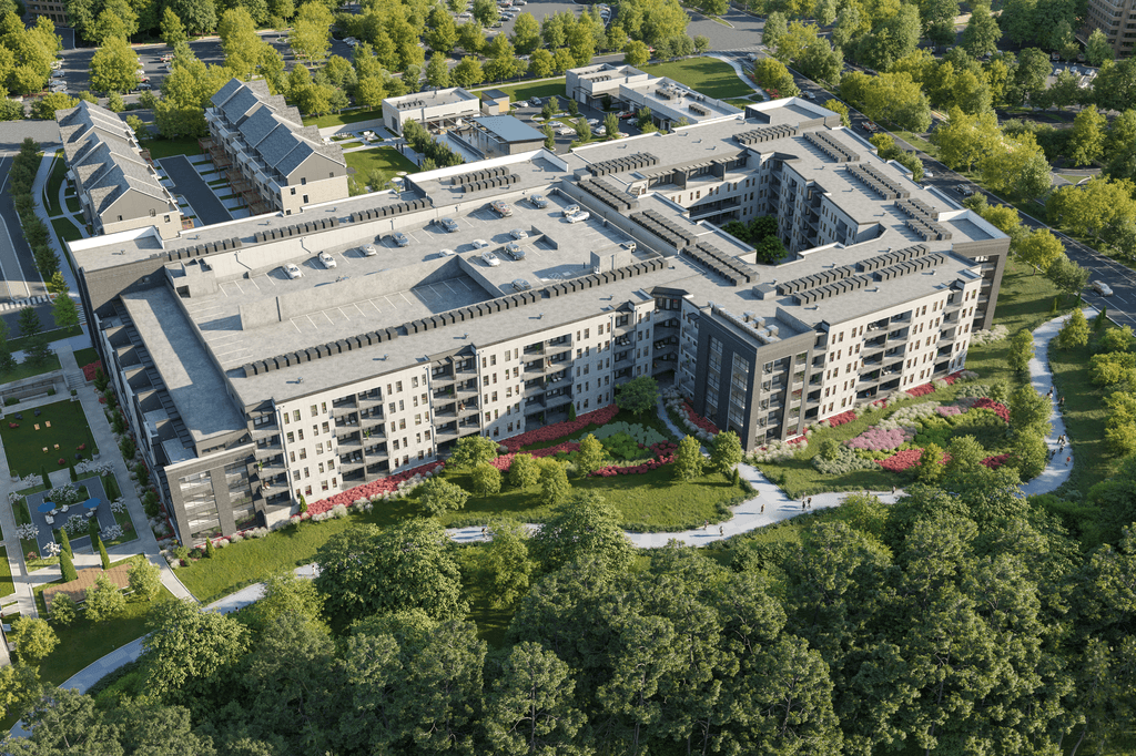 A large, multi-story building with a grey roof and white walls is surrounded by a green landscape.