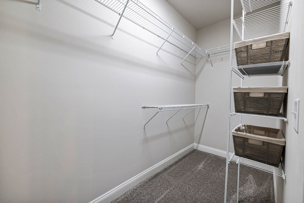 interior model walk in closet with white walls and a white closet with baskets and wire shelves