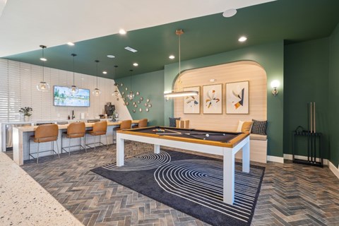 A billiard table is in the middle of a room, with a bard and TV behind.