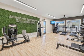 A gym with a green wall that says "Strive for progress not perfection" and a row of treadmills.