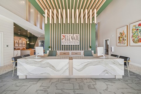 A reception area with a white reception desk and a green wall with a sign that says "Elevate Riverview".
