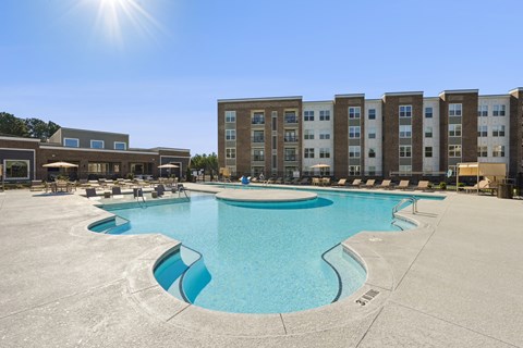 A large swimming pool in front of apartment buildings on a sunny day.