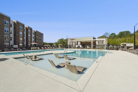 A large swimming pool with lounge chairs in front of apartment buildings.