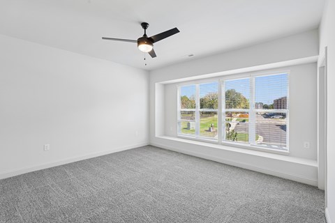 A room with a ceiling fan and a window showing a view of a residential area.