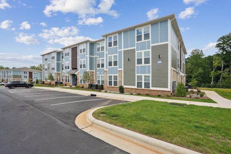 A modern apartment complex with a parking lot in front.