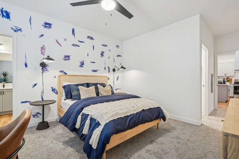 A bedroom with a bed, a ceiling fan, and a wall with blue paint splatters.