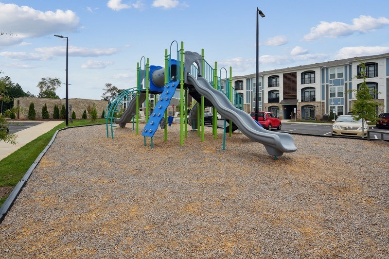 A playground with a blue and green slide in the foreground and apartment buildings in the background.