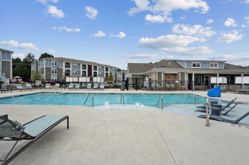 A large outdoor swimming pool with lounge chairs and a building in the background.