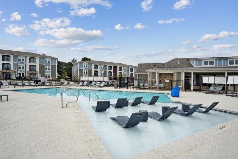 A large outdoor swimming pool with lounge chairs and apartment buildings in the background.