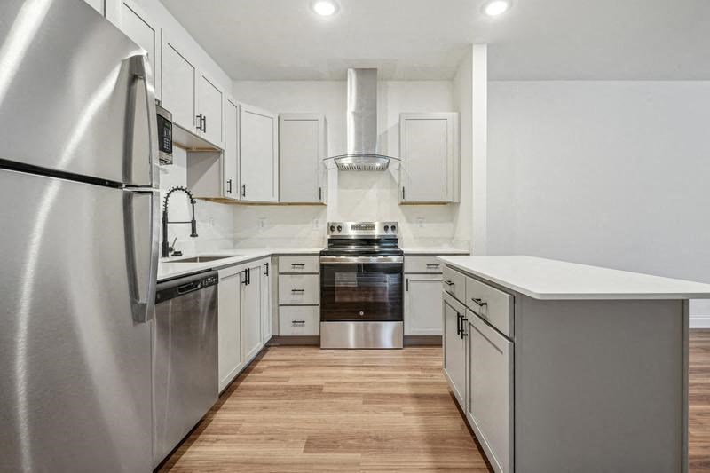 A modern kitchen with a stainless steel refrigerator and wooden floors.