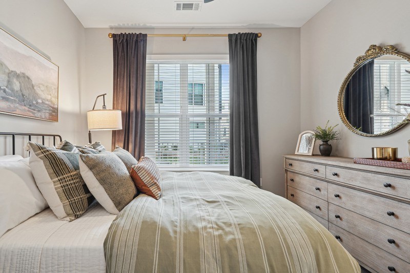 A bedroom with a large bed, a dresser with a mirror, and a window with curtains.