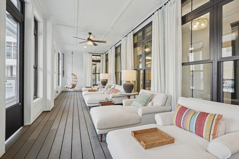 A long, narrow living room with white furniture and a wooden floor.