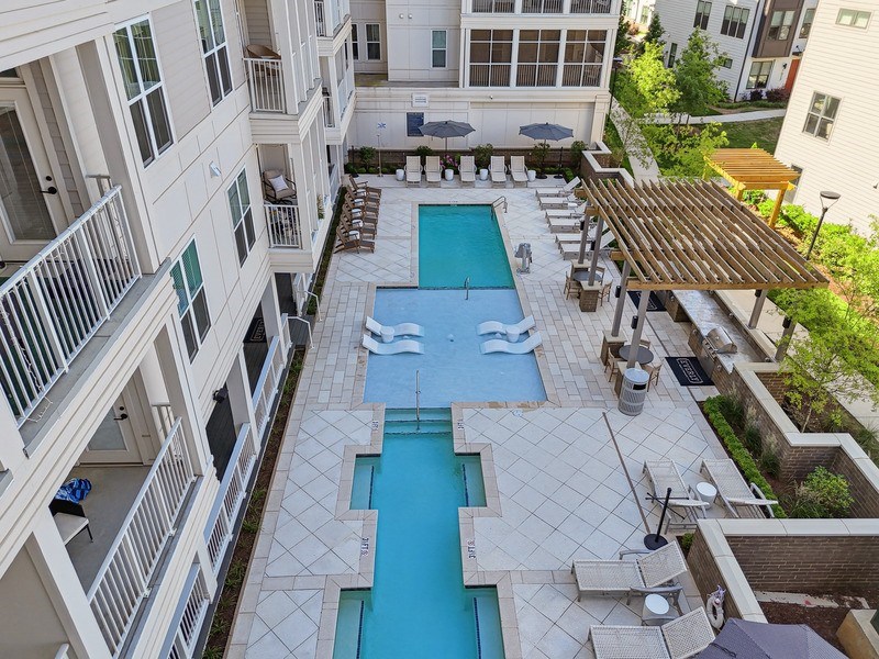 A large swimming pool surrounded by an apartment building and a patio.