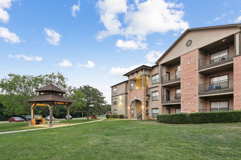 a gazebo sits in the grass next to an apartment building