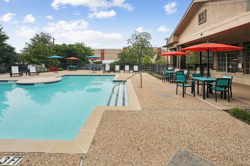 a swimming pool with tables and umbrellas outside of a building