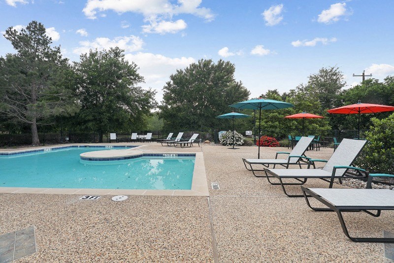 a swimming pool with chairs and umbrellas on a clear day