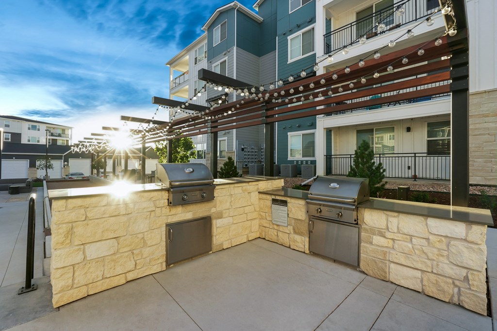 an outdoor kitchen with a stone wall and two barbecue pits in front of a building
