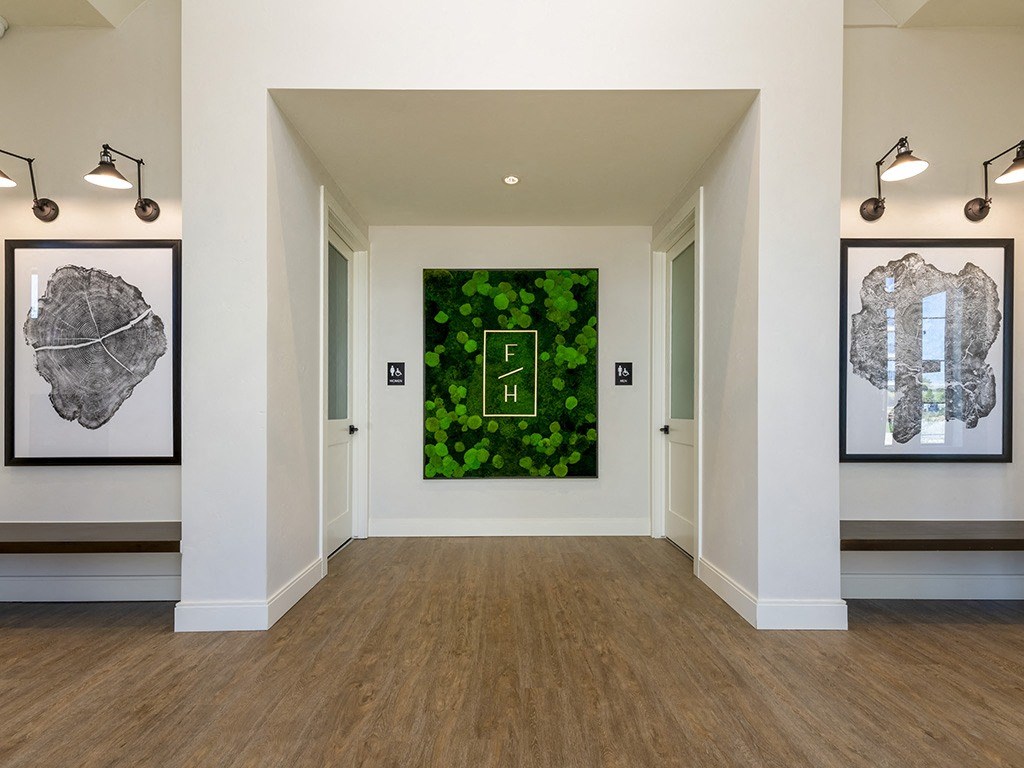 a gallery with a wall of green plants and paintings