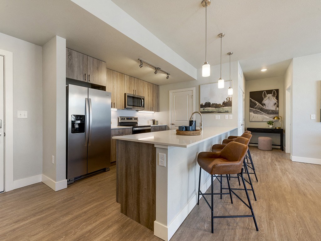 A kitchen with a refrigerator, stove, and bar stools.