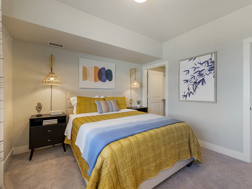 A bedroom with a bed, nightstand, and artwork on the wall.