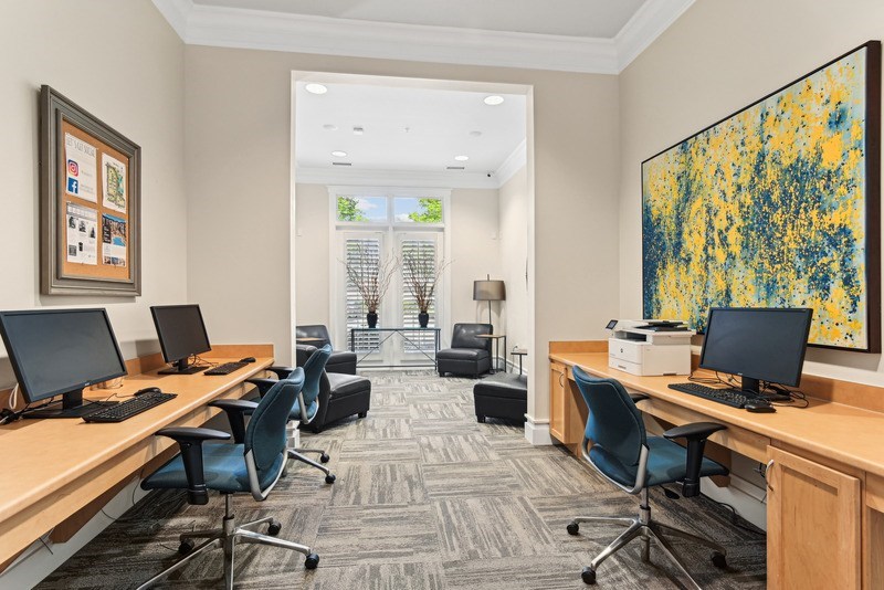A room with a carpeted floor, a desk with a computer, a chair, and a painting on the wall.