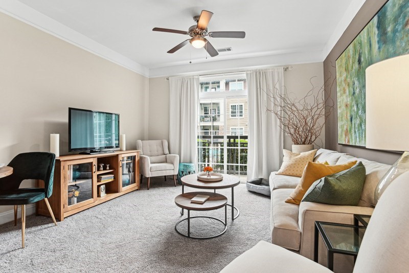 A living room with a white couch, a wooden cabinet, a glass coffee table, and a ceiling fan.