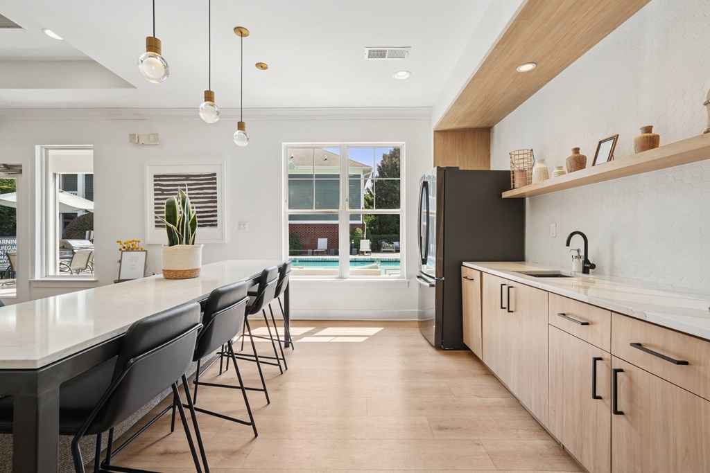 A modern kitchen with a long white island and black chairs.
