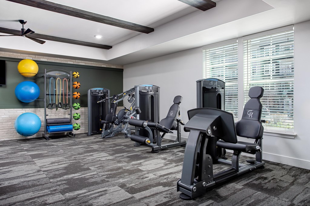 A gym with a variety of equipment including a treadmill, a stationary bike, a rowing machine, a weight bench, and a ceiling fan.