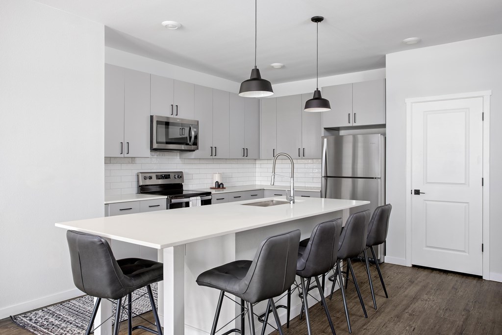 A modern kitchen with a white island and grey chairs.