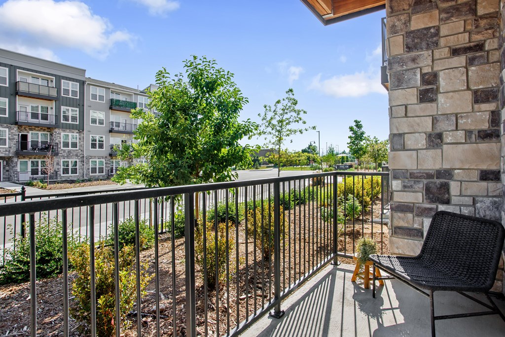 A balcony with a black chair and a table with a vase of flowers on it.