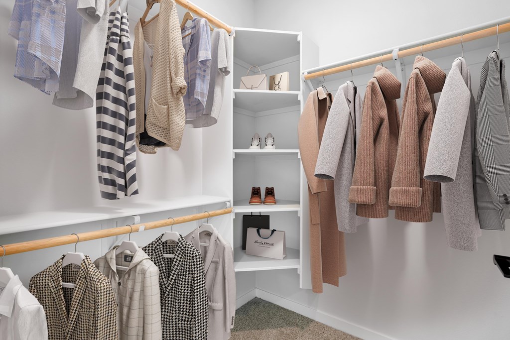 A white closet with clothes hanging and shelves with shoes and boxes.