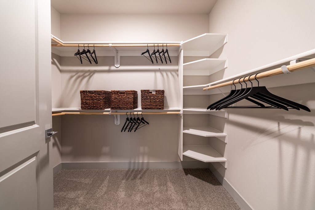 A walk in closet with white shelves and baskets.