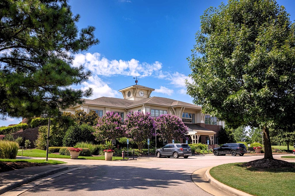 A large house with a clock tower on the roof is surrounded by a well-manicured lawn and trees.