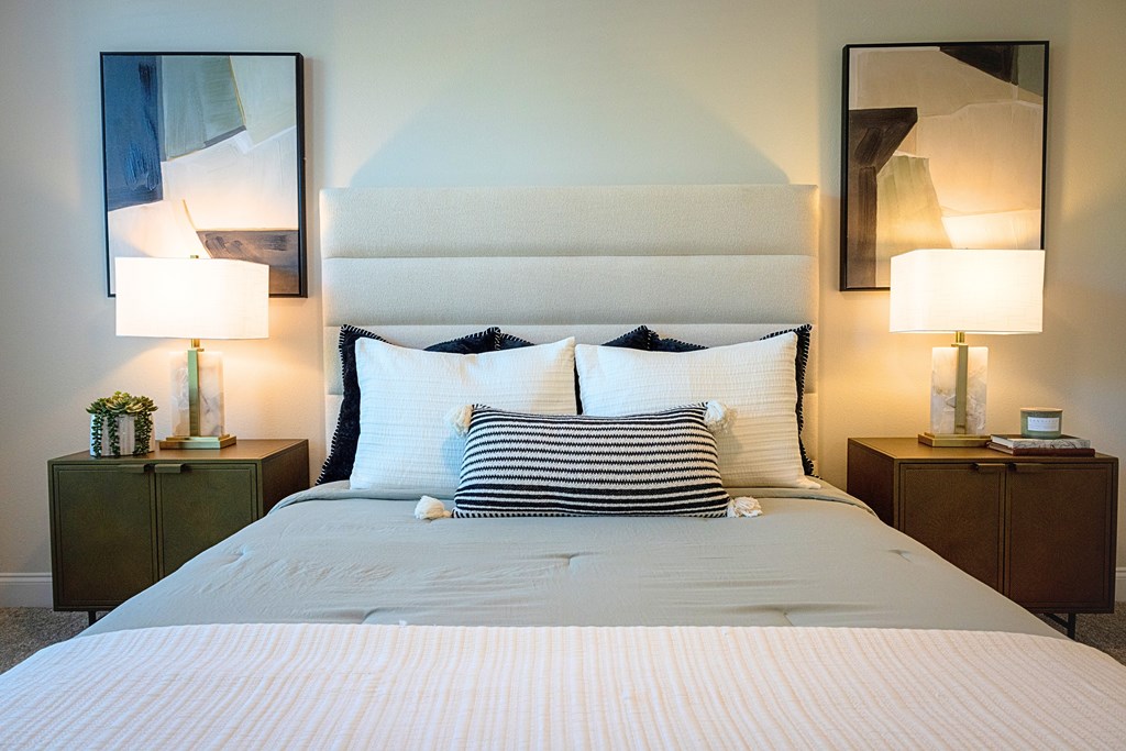 A bed with a white headboard and striped pillows is flanked by two lamps on wooden nightstands.