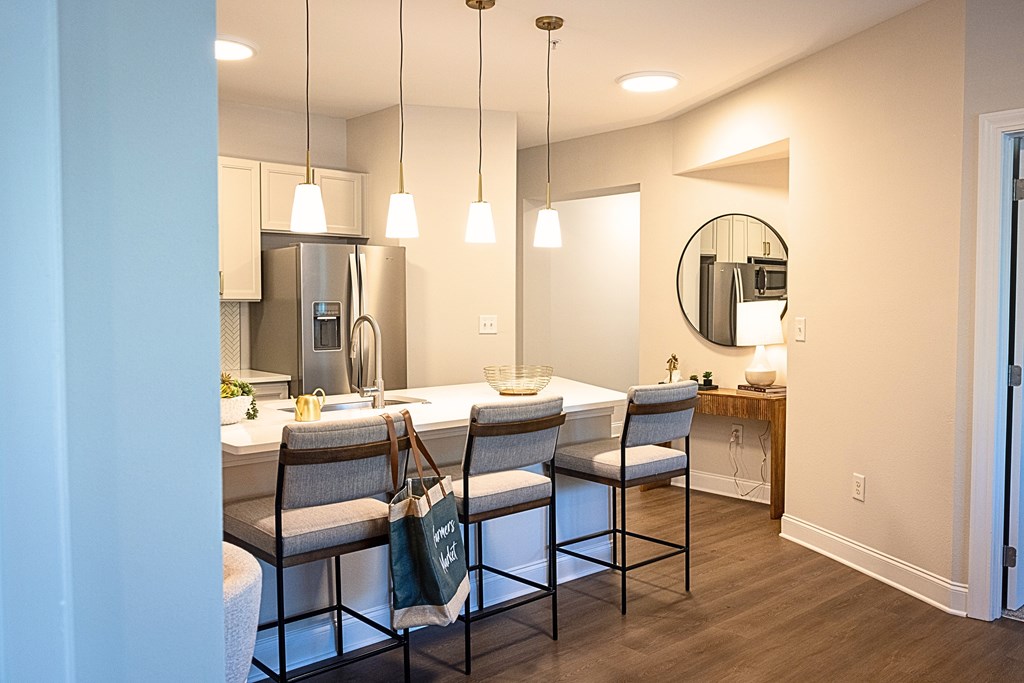 A kitchen with a refrigerator, sink, and chairs.